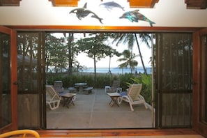 A view through a glass door to a patio area with outdoor furniture, palm trees, and a view of the ocean.