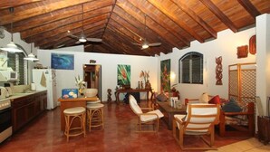 Un'ampia zona giorno con soffitto alto, travi in legno, un tavolo da pranzo con sedie, angolo cottura con elettrodomestici e opere d'arte alle pareti.