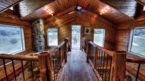 Interior de madera con una escalera central de madera, paredes de piedra y amplios ventanales que ofrecen vistas al exterior.