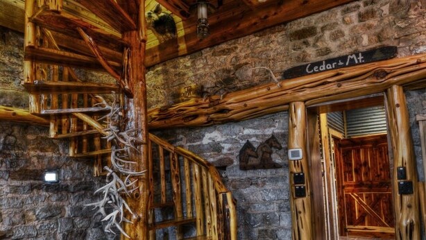 Un interior rústico con una escalera de caracol de madera, paredes de piedra y un cartel que dice "Cedarl & Mt". 
