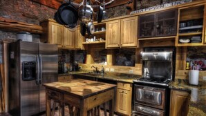 Una cocina rústica con armarios de madera, un refrigerador de acero inoxidable, una estufa y ollas colgantes.