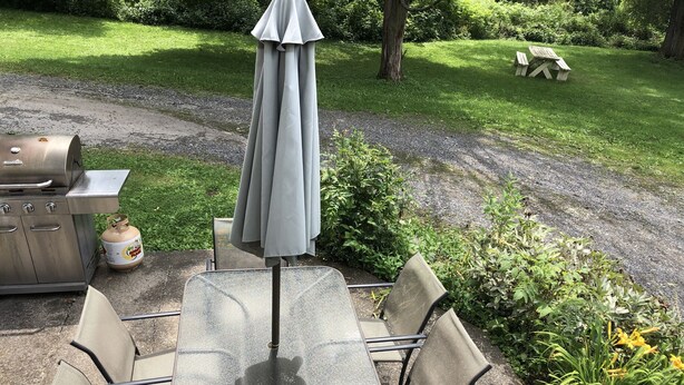 Een terras buiten met een tafel, stoelen, een barbecue en een gasfles.