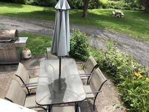 Eine Terrass mit Tisch, Stühlen, einem Grill und einem Gasbehälter.