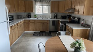 Een moderne keuken met houten kastjes, roestvrijstalen apparatuur en een eethoek met een tafel en stoelen.
