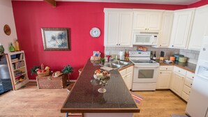 Cucina con mobili bianchi, un forno a microonde e un fornello. La parete è rossa e il pavimento in legno.