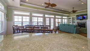 A spacious living room with a large dining table, multiple ceiling fans, and a fireplace. - Custom Home With Many Extras with beautiful Ocean Views! (Ocean Isle Beach)