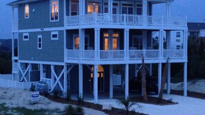 A two-story beachfront house with multiple balconies, a covered front porch, and a sandy driveway. - Custom Home With Many Extras with beautiful Ocean Views! (Ocean Isle Beach)