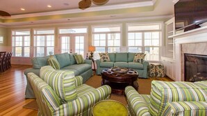 A spacious living room with a large green sofa, striped armchairs, a round coffee table, and a fireplace. - Custom Home With Many Extras with beautiful Ocean Views! (Ocean Isle Beach)