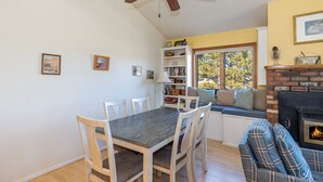 A dining area with a table and chairs, a bookshelf, a window seat, and a fireplace.
