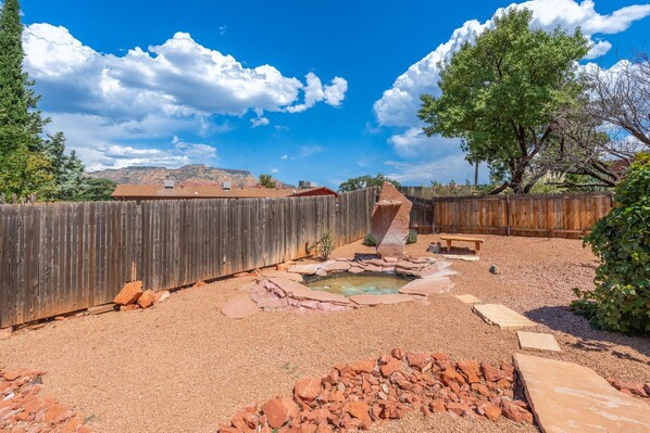 A backyard with a wooden fence, a small pond, and a stone pathway.