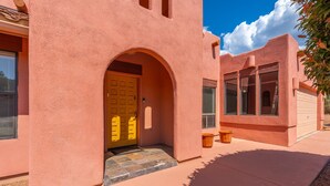 A pink stucco house with a yellow door, a small porch, and a garage. - Waterfall, Grapevines and Hot Tub with Views - Nice House Too! (Sedona)