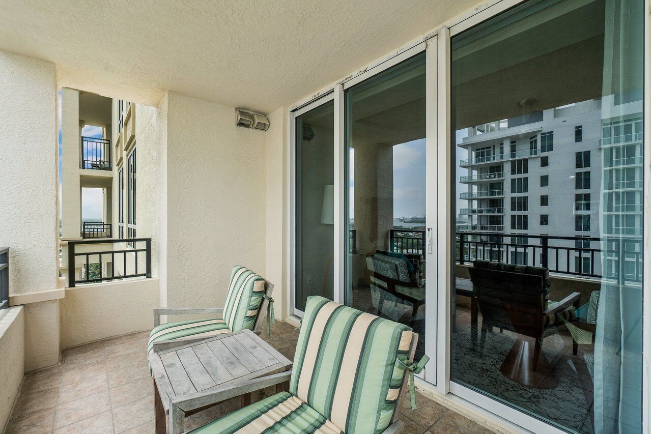 A balcony with a wooden table and striped chairs, a sliding glass door, and a view of a building with multiple balconies.