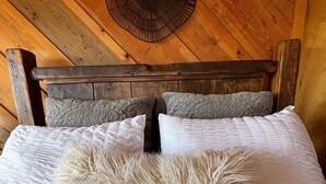 Een bed met een zacht kussen, een houten hoofdbord en een ronde wandventilator.