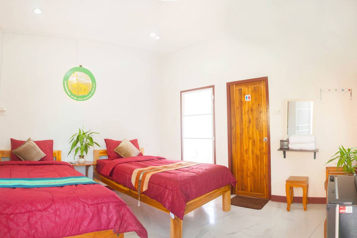 Habitación de hotel con dos camas, una puerta de madera, una mesita con una tetera y un espejo en la pared.