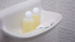 Un lavamanos de cerámica blanca con dos botellas de jabón amarillo y una toalla de papel blanca.