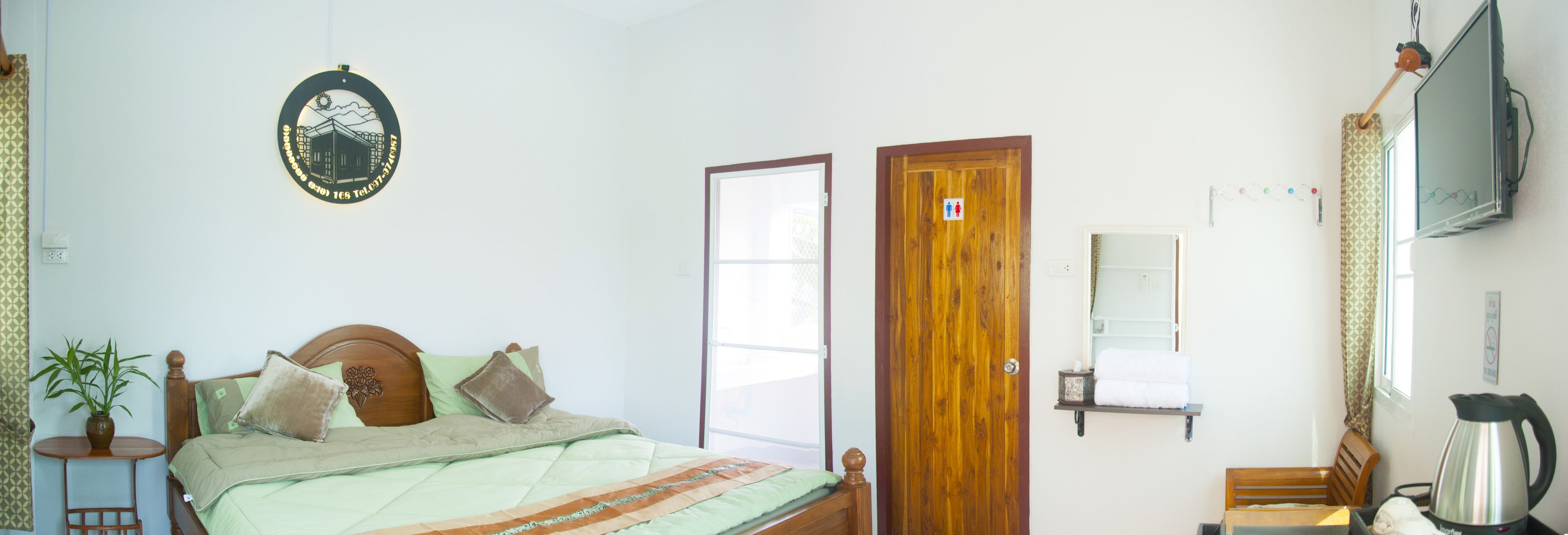 A bedroom with a bed, a wooden door, a television, and a wall-mounted shelf.