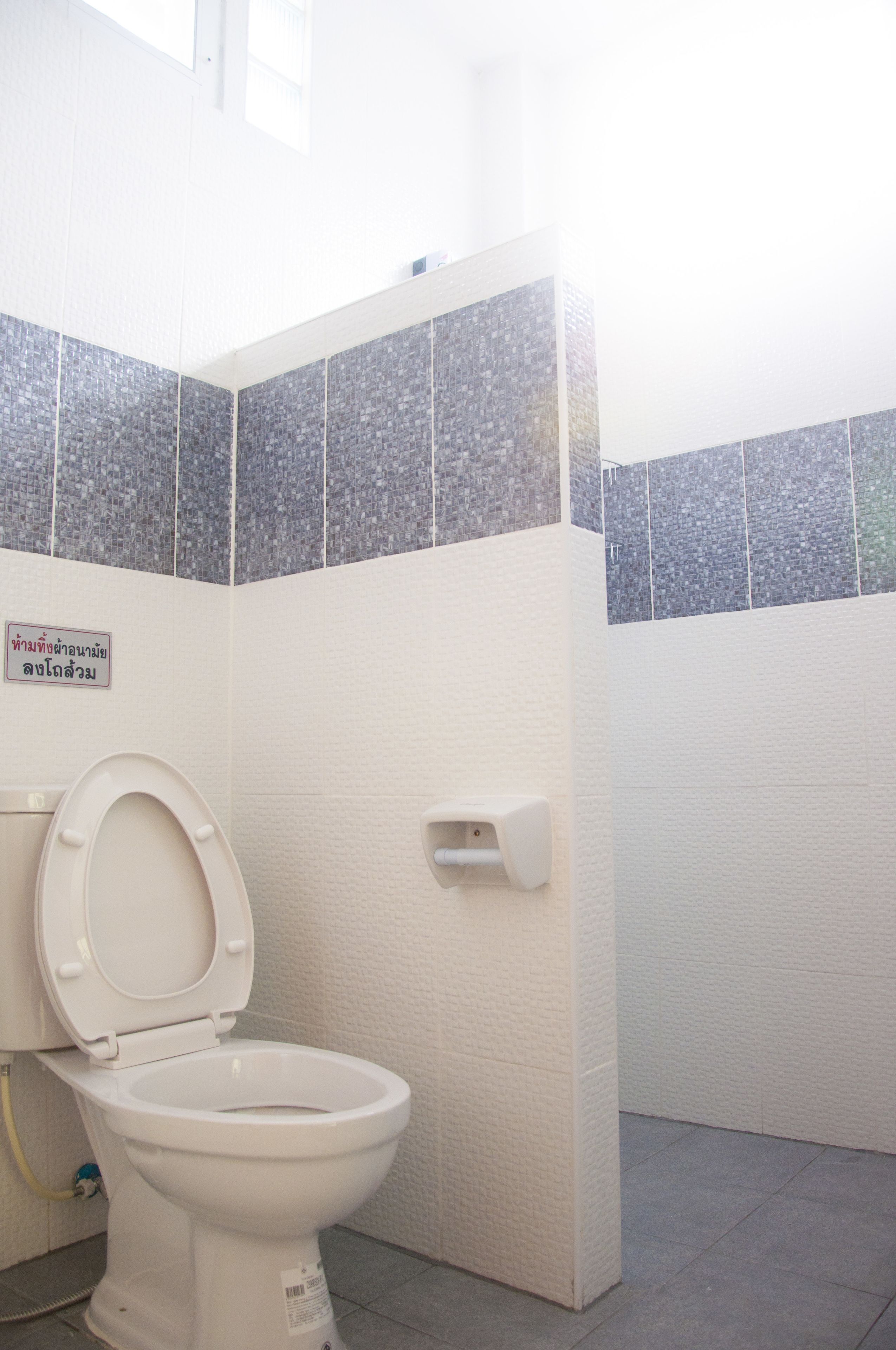 Un baño con un inodoro blanco, un secador de manos y un letrero en un idioma extranjero.