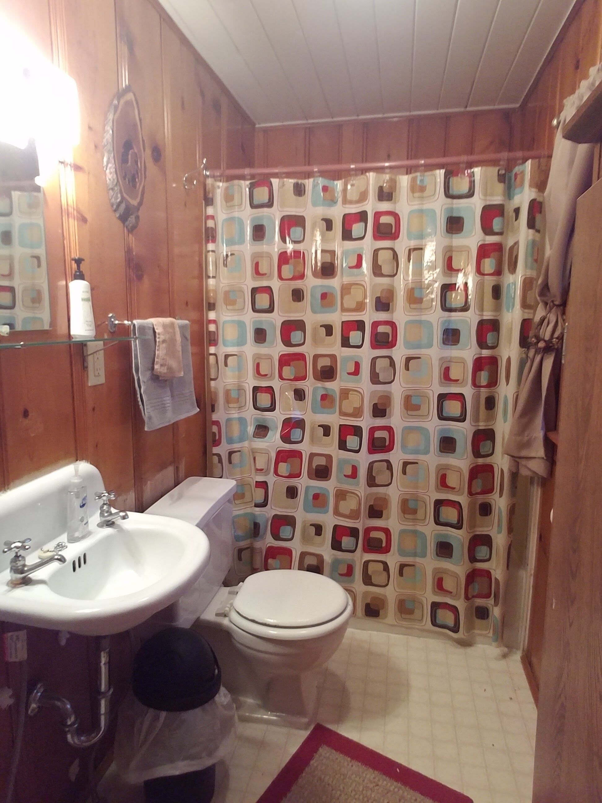Une salle de bain avec un intérieur en bois, un lavabo blanc, des toilettes et un rideau de douche à motifs géométriques.
