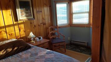 A bedroom with a bed, a chair, a nightstand, a lamp, and a window with blinds.