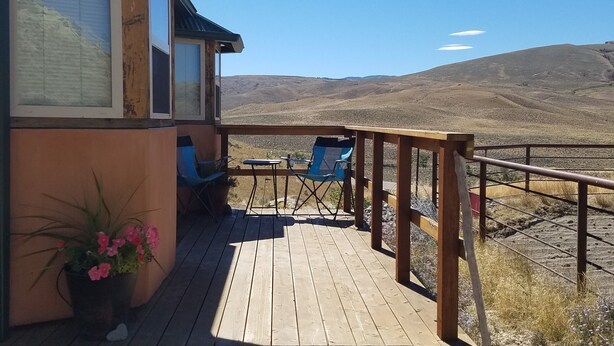 Una terraza de madera con barandilla, una planta en maceta y una silla azul.