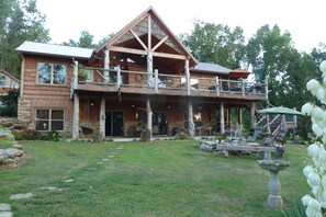 A two-story log cabin with a balcony, outdoor seating area, and a stone foundation.