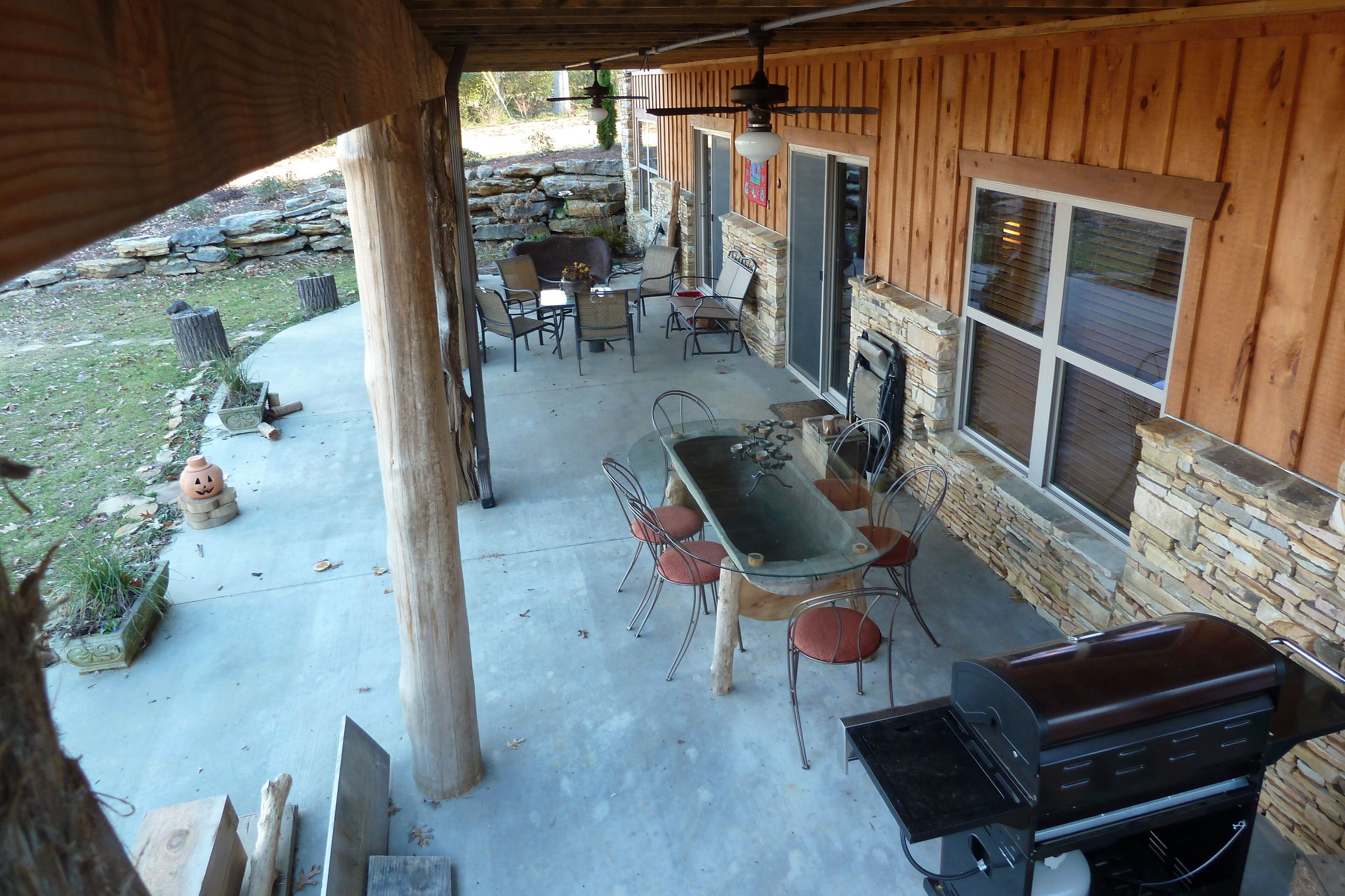 A covered patio with a barbecue grill, outdoor seating, and a stone wall.