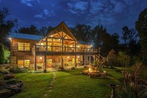 Une grande cabane en rondins à plusieurs étages, dotée d’un balcon imposant, entourée d’un jardin bien entretenu et d’un foyer.