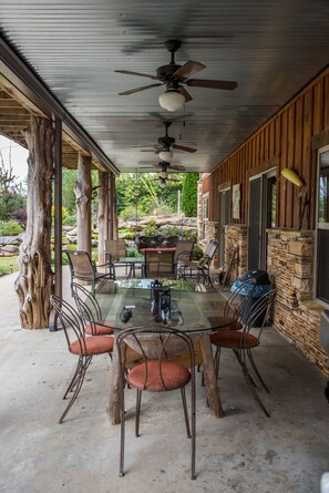 A covered patio with a glass table and chairs, a ceiling fan, and stone walls.