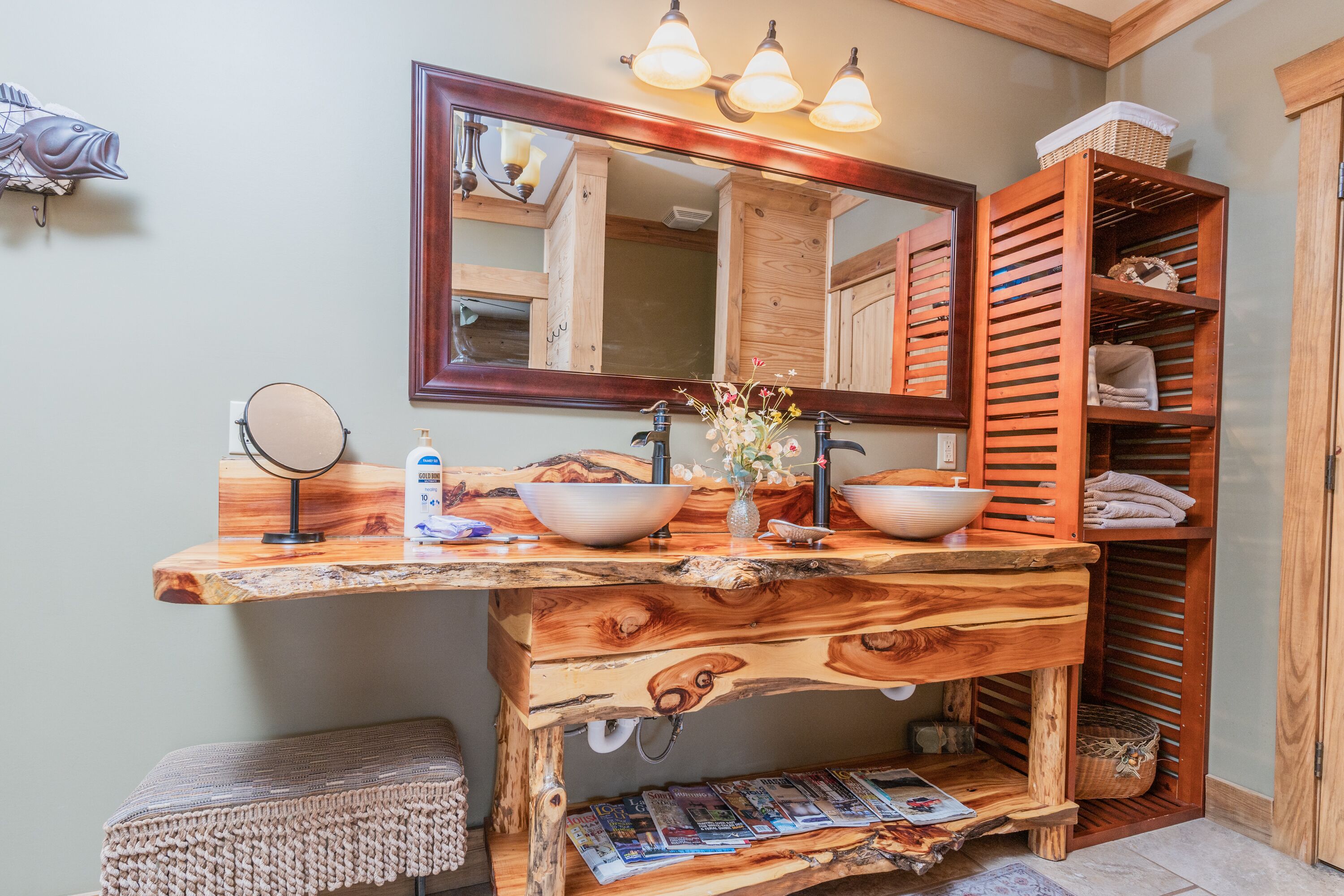 Une salle de bain avec un meuble-lavabo en bois, deux vasques, un miroir et une étagère avec des serviettes.