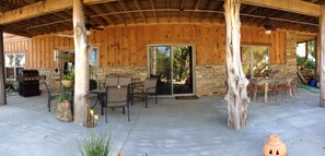A covered patio area with a stone fireplace, outdoor seating, and a grill.