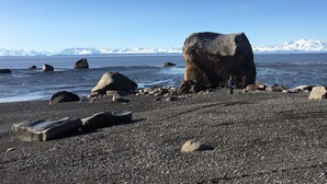 A rocky beach with large boulders and a clear view of snow-capped mountains in the distance. - Your "Home Away From Home"-Rustic Alaskan Home (Soldotna)