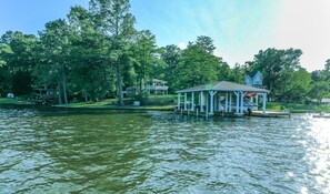 Un gazebo sul lago con un molo che si protende nell'acqua, immerso nel verde e con una grande casa sullo sfondo.