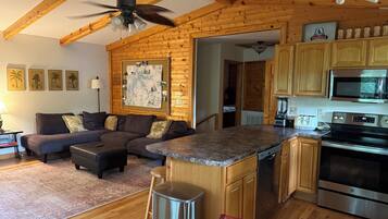 A spacious living area with a wooden ceiling, a large island with a built-in microwave, and a kitchen with wooden cabinets and stainless steel appliances.