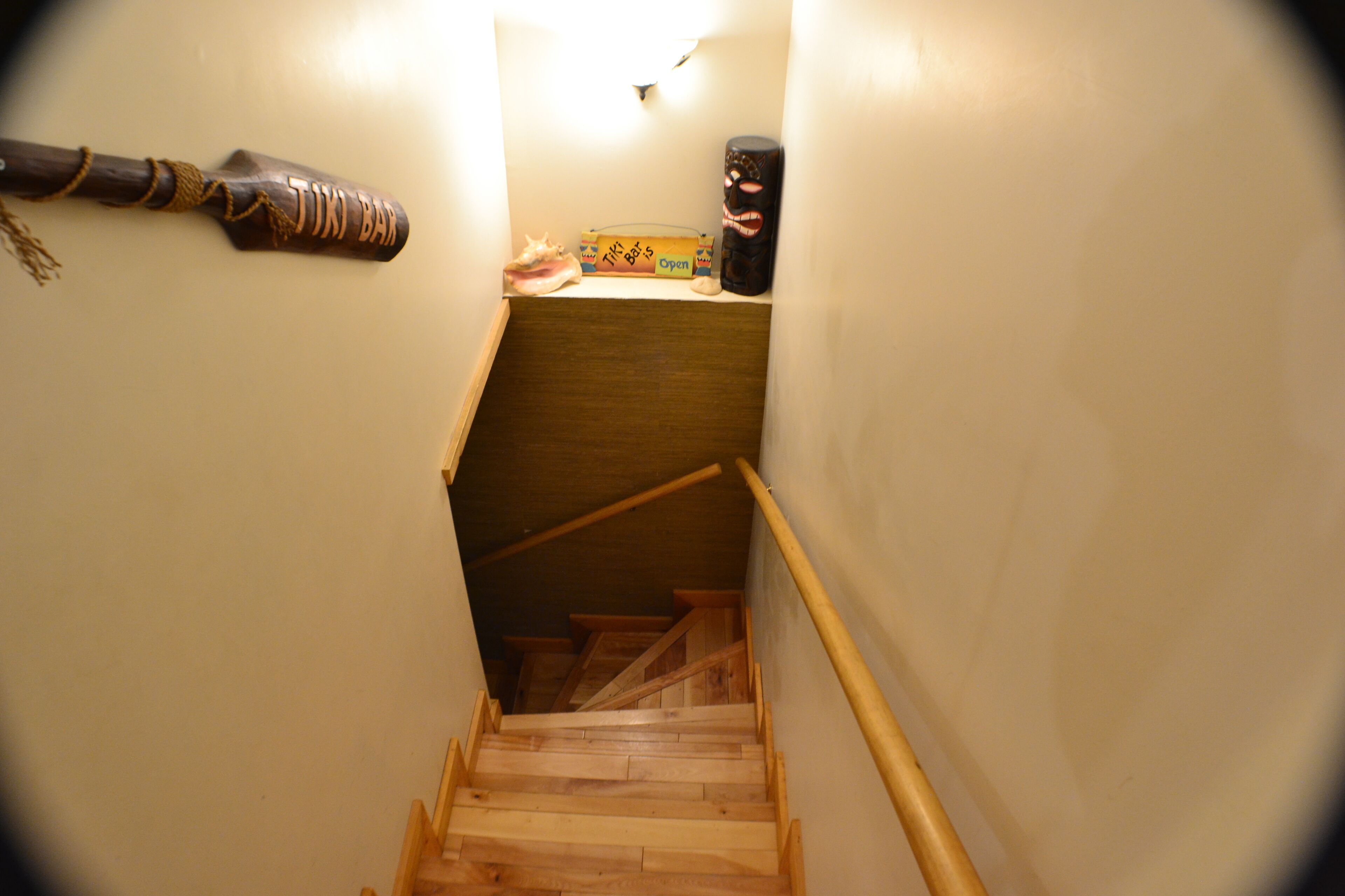 A narrow stairway leading to a lower level with a wooden handrail and a small shelf with items on it.