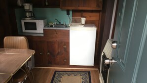 A compact kitchen with a microwave, sink, and refrigerator. There is a dining table with chairs and a patterned rug.