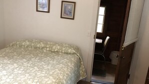 A bedroom with a bed, two framed pictures on the wall, a door leading to another room, and a wooden floor.