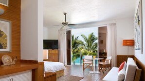 Une chambre d’hôtel équipée d’un lit, d’un bureau, d’une chaise, d’un canapé, d’un ventilateur de plafond et offrant une vue sur des palmiers et une piscine.