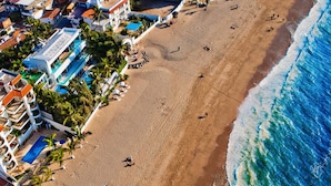 Une vue aérienne d’une plage avec des bâtiments, des palmiers et des personnes.