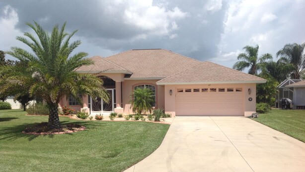 A single-story house with a garage, a driveway, and a well-maintained lawn with palm trees.