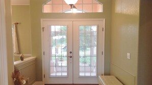A hallway with a double door, a bench, a vase with dried flowers, and a window with blinds.