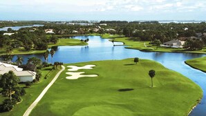 A golf course with a water hazard, a walking path, and surrounding greenery.