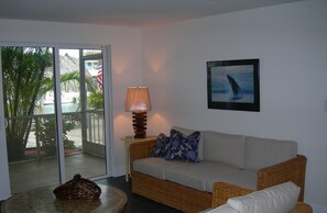 Relax in this inviting living room with a wicker sofa, coffee table, and wall-mounted lamp. Enjoy the view of palm trees and a pool through the sliding glass door.