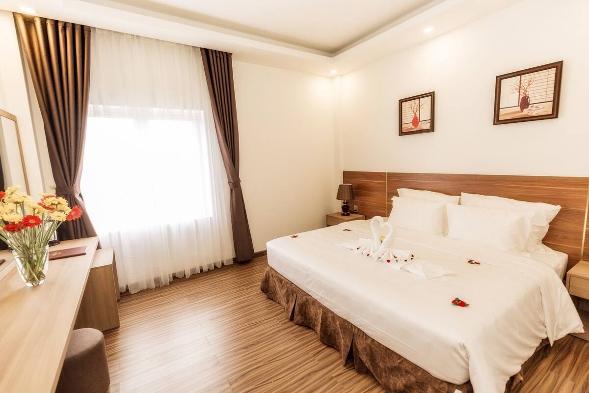A hotel room with a large bed, a desk with a vase of flowers, and two framed pictures on the wall.