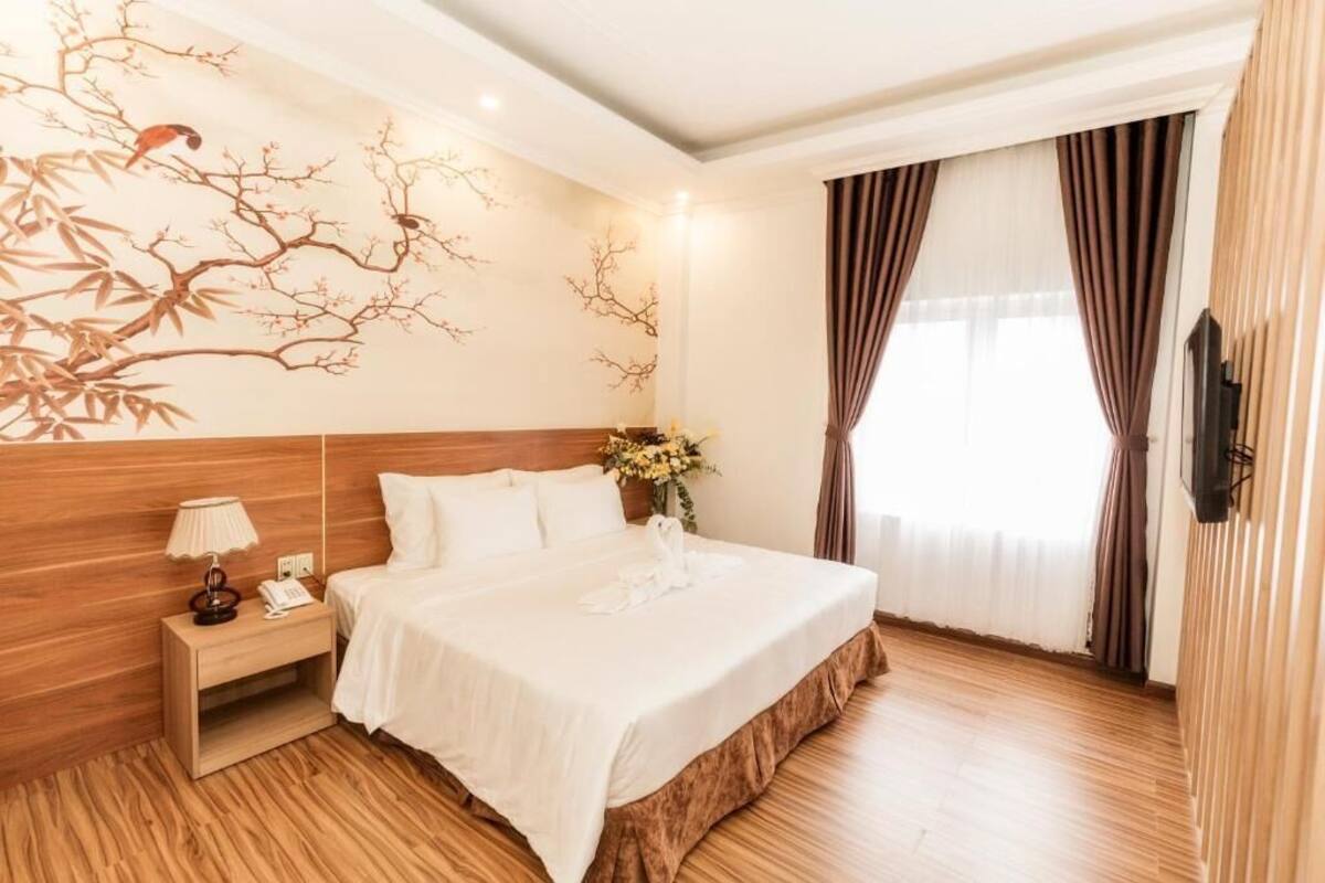 A hotel room with a wooden headboard, a bed with white linens, a nightstand with a lamp, and a wall mural.