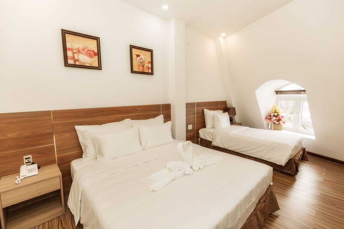 A hotel room with two beds, wooden headboards, white bedding, a bedside phone, and framed artwork on the wall.