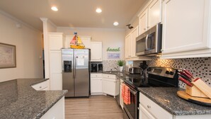 A modern kitchen with white cabinets, a stainless steel refrigerator, a microwave, and a stove. - Immaculate, 4 Bedrooms/4 Bath, w/ Pool, Exterior Elevator and Golf Cart (Emerald Isle)