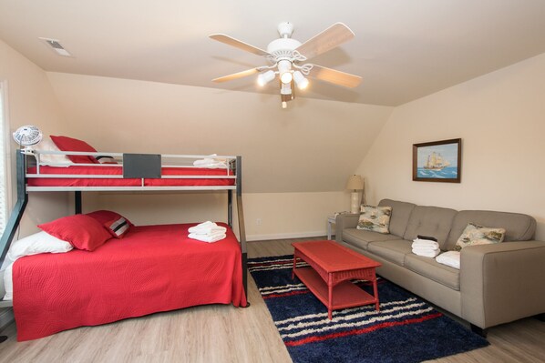 A room with bunk beds, a sofa, a small table, a ceiling fan, and a painting on the wall. - Immaculate, 4 Bedrooms/4 Bath, w/ Pool, Exterior Elevator and Golf Cart (Emerald Isle)