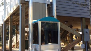 A house with a covered outdoor area, a staircase, and a metal structure. - Immaculate, 4 Bedrooms/4 Bath, w/ Pool, Exterior Elevator and Golf Cart (Emerald Isle)