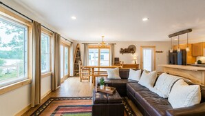Ein geräumiges Wohnzimmer mit einer großen Eckcouch, einem Essbereich mit Holztisch und Seeblick durch große Fenster.