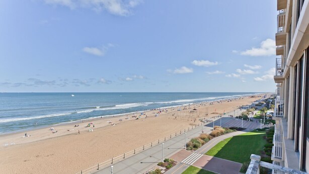 A beach view from a balcony overlooking a sandy beach with a clear sky. - Oceanfront & Pool, on the Boardwalk at 37th Street (Virginia Beach)